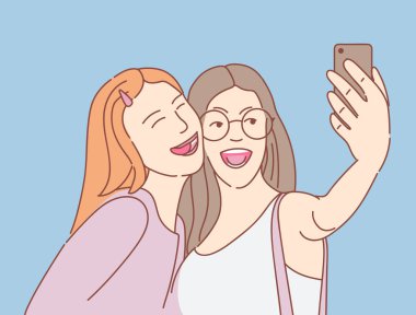 mavi arka planda akıllı telefon ile selfie çeken iki mutlu genç kız
