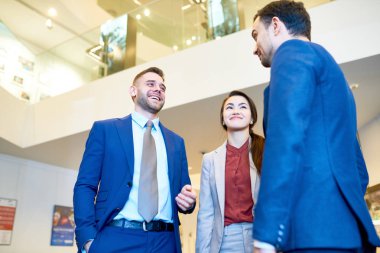 Grup mutlu modern ofis binası içinde sohbet ederken gülümseyen neşeli genç iş adamları düşük açılı manzaraya