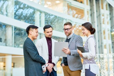 Geniş ofis lobisinde ayakta ve gayrı resmi çalışma toplantısı yaparken istatistik verileri analiz finansal yöneticilerinin etnik grup