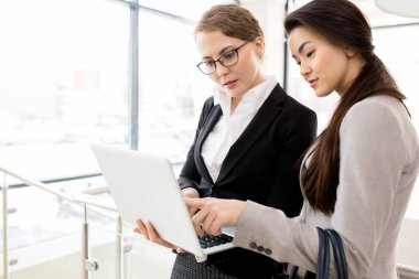 Geniş ofis lobisinde ayakta ve dizüstü bilgisayar, arka plan üzerinde panoramik pencerelere yardımıyla ile başlangıç proje üzerinde beyin fırtınası çalışkan yöneticileri çok etnik gruptan oluşan takım