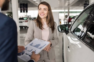 Bel kadar mutlu bir şekilde lüks araba showroom seçerken araba satıcısı için dinleme gülümseyen modern genç kadın portresi
