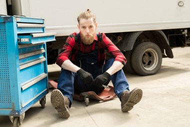 Otomatik mekanik sarmaşık hizmet garaj ve kameraya bakıyor kırık kamyon yakınındaki oturan genç yakışıklı portresi sakallı