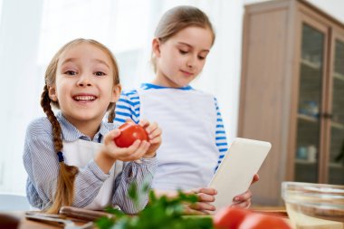 İki kız kardeş birlikte mutfakta yemek portresi ripe domates tutan mutlu küçük kız üzerinde odaklanmak ve kameraya, seyir alanı kopyalayın