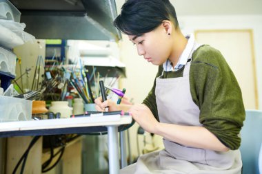 Yan görünüm portre çizim Genç Asyalı kadın glassworking atölye çalışmasında, güzel takı oluşturmak hazır skeçler