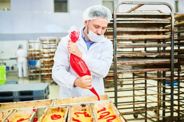 集中製菓工場労働者で 白衣のアイシング バッグから赤いクリームを絞る — ストック写真