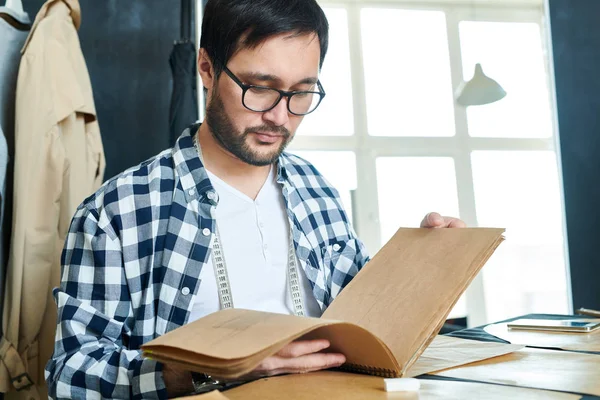 Joven Sastre Sentado Escritorio Salón Mirando Través Cuaderno Bocetos Papel —  Fotos de Stock