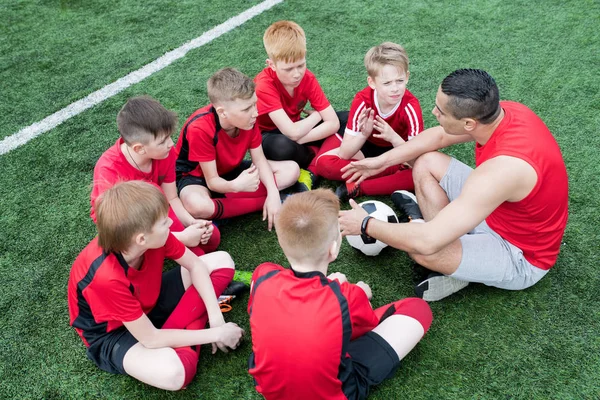 坐在圈子里的男孩的高角度肖像听激励士气的教练在团队练习前的谈话 — 图库照片