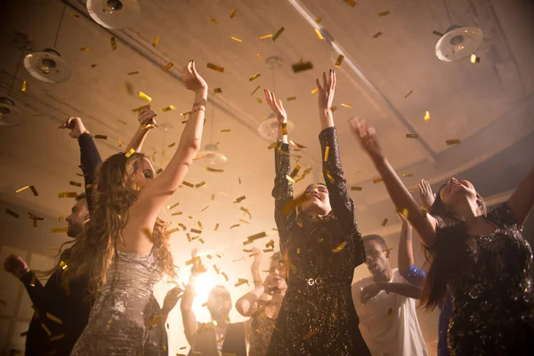 一群快乐的年轻男女在时尚夜总会玩耍的同时 举起双手跳舞 金色的五彩纸屑在空中飞翔 — 图库照片