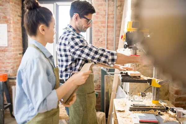 Side view portrait of two modern artisans collaborating on crafting project in woodworking shop