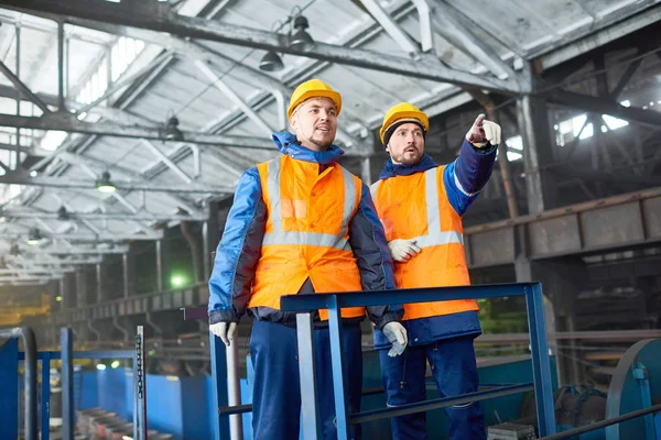 制服を着て一生懸命に働く技術者のチーム Hardhats 直面している問題を議論しながら 近代的な工場の生産部門を見て それらの つは何かを指して — ストック写真