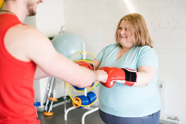 Portrait of happy fat woman fist bumping with personal fitness  instructor celebrating success in training