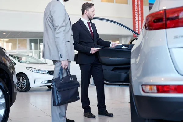 Car salesman representing new car to male customer at auto showroom