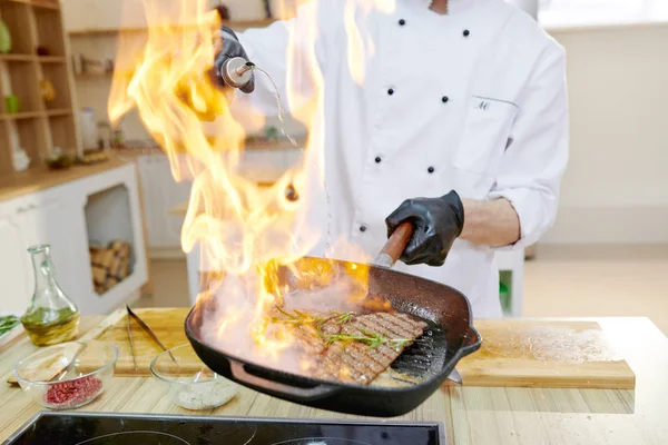 Closeup of flaming frying pan in hands of professional chef cooking in modern restaurant kitchen, copy space