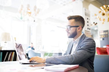 Yan görünüm portre yakışıklı iş Yöneticisi küçük Dükkanı, kopya alanı çalışırken dizüstü bilgisayar kullanarak