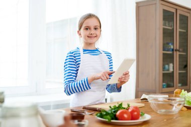 Yeni video üzerinde çalışma ve onun takipçileri sağlıklı salata, arka plan üzerinde geniş mutfak iç hazırlamak nasıl açıklayan önlük giyen küçük gıda blogger