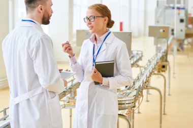 Beyaz önlük ve modern süt fabrikasının tur verirken sakallı yatırımcıya üretim süreci açıklayan gözlük takıyor çekici sarışın fabrika işçisi