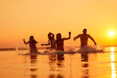 Su çevrelerindeki sunset beach, eğlenirken suda çalışan neşeli duygusal genç arkadaşlar