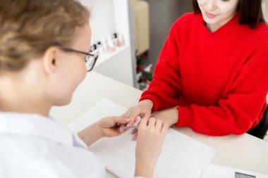 Beyaz önlük oturma gülümseyen müvekkili karşısında tırnaklarını Lehçe uygulamadan önce dosyalama iken giyen genç manikürcü