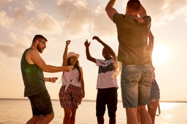 Neşeli kendinden geçmiş genç çok ırklı arkadaşlar geçici zevk yaz parti giyim ve el eller denizde dans