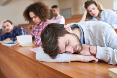 Yorgun yakışıklı genç öğrenci çocuk sakallı yorgun sıkıcı ders Üniversitesi masanın üzerine eğilerek ve sınıfı kapalı gözler ile uyku