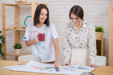 Genç tasarımcılar birlikte ahşap masasında duran umut verici proje üzerinde gülümseyen, onlardan biri hoş kokulu kahve keyfi