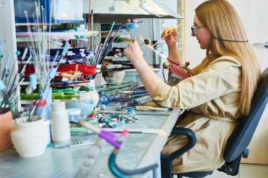 Yan görünümü portresi glassworking Studio'da güzel el yapımı takı boncuk yaparken Gaz Meşalesi tarafından cam şekillendirme genç kadın sanatçı