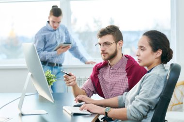 Beyaz kadın yöneticisi bilgisayarda modern ofiste otururken genç erkek çalışan öğretim