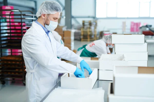 製菓工場労働者白いコートに立って 空の紙箱の準備の側面図 — ストック写真