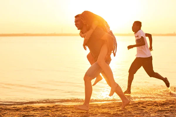 Jovem Alegre Hilariante Carregando Namorada Nas Costas Andando Sobre Praia — Fotografia de Stock