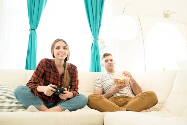 积极集中的年轻女子使用游戏杆 而玩视频游戏她的男朋友对游戏吃爆米花和欢呼为女朋友在家中的乐趣 — 图库照片