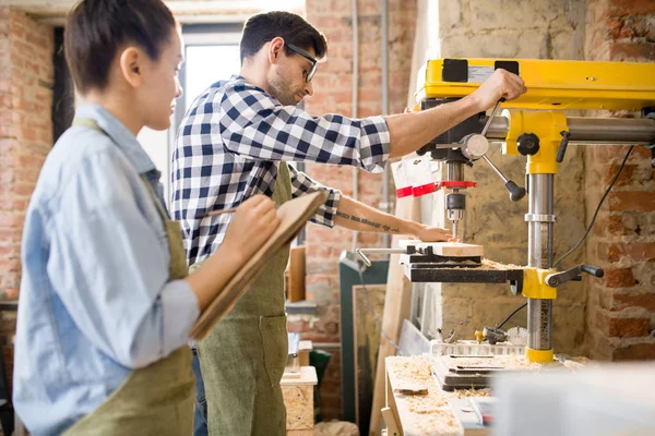 Side view portrait of  two modern artisans, man and woman, working together using machines in woodworking shop, collaborating on creative project