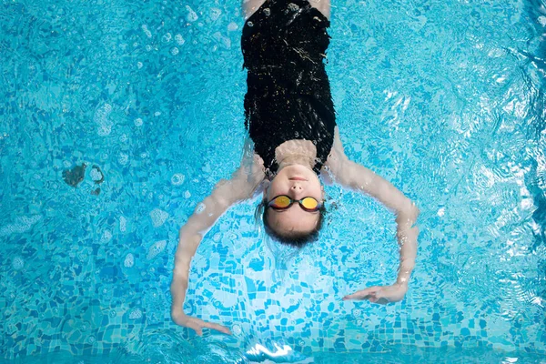 Gözlük ve yüzme havuzunda su üzerinde yüzen atletik mayo giyen ciddi sakin kız görünümünü yüksek açı