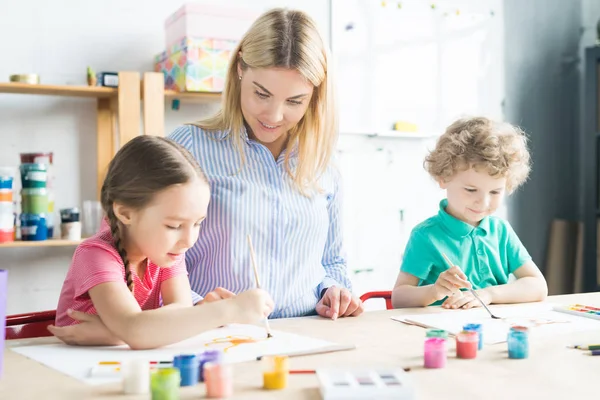 人の子供 男の子と女の子 美術の授業でテーブルで 美術の先生と共に絵画 — ストック写真