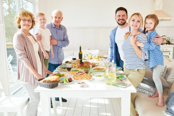 Portrait of happy two generation  family enjoying dinner together posing round festive table with delicious dishes and smiling at camera in modern sunlit apartment, copy space