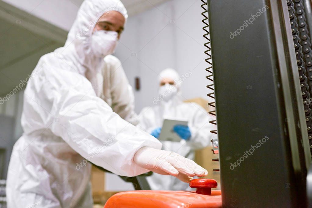 Sports nutrition production worker in protective clothing pushing button on pallet truck. 