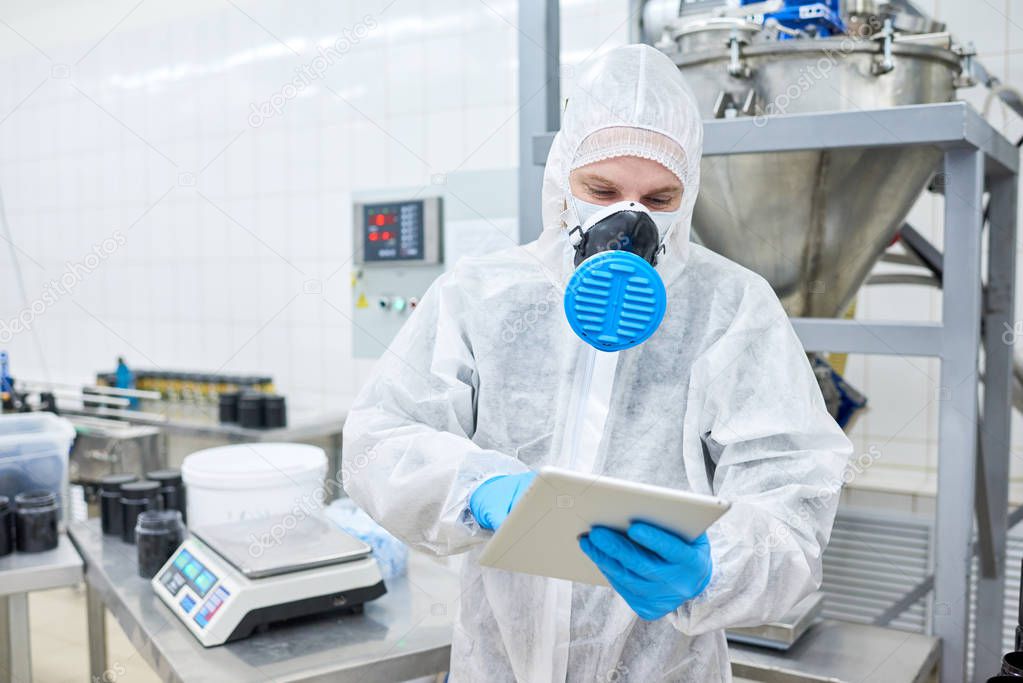 Sports nutrition production employee working in protective clothing using tablet computer.