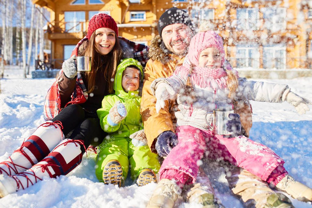 Caucasian family with two little children having fun outdoors, throwing up snow, drinking hot tea and smiling cheerfully