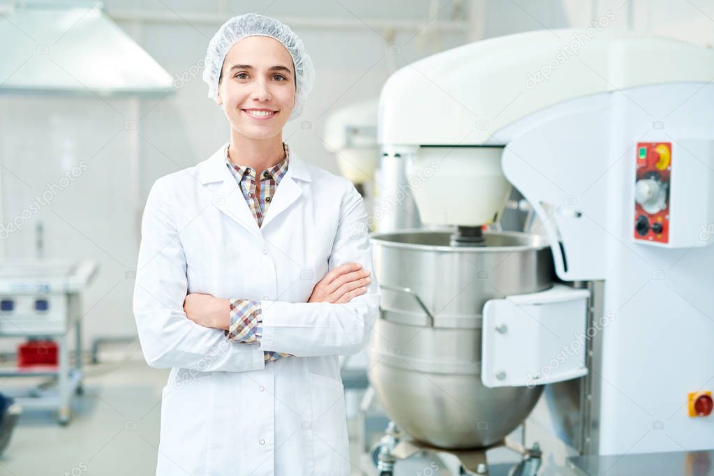 Beautiful confectionery factory worker standing in white coat with arms crossed smiling and looking at camera.