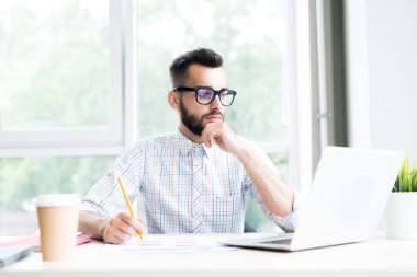 Resepsiyon düşünceli dizüstü bilgisayar ekranına, kopya alanı bakarak ofiste çalışan yakışıklı sakallı işadamı portresi
