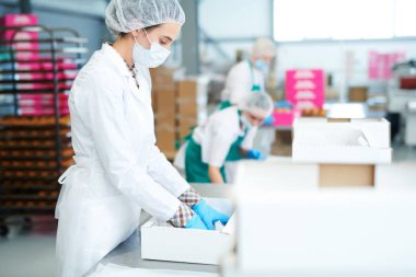 Kırpma Şekerleme fabrikası çalışan beyaz ceket pişirme parşömen boş kağıt kutusu koyarak yan görünüm. 