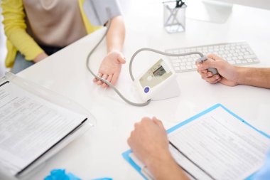 Tanınmayan Doktor masada oturan ve elektronik monitör aygıtı kullanarak bayan hasta kan basıncı ölçme closeup