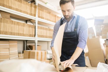 Orta yaşlı işçi ekose desenli gömlek ve basınç güç çeviriciler dururken geniş depo ekipman fabrika ölçme ambalaj tulum giyen sakallı