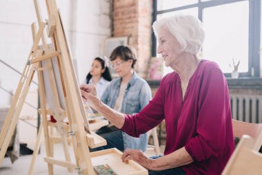 Yan sırada oturan ve sanat atölyesi, gülümseyen kadın kıdemli odaklanmak Sephalar, resim sanat öğrencileri görünümü portresi