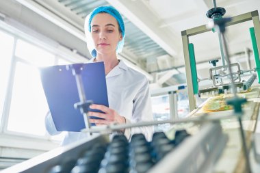 Laboratuvar giyen genç bir kadın işçi portresi düşük açılı güç üniteleri beklemede ceket ve temiz üretim atölyesinde panosuna yazma alanı Kopyala