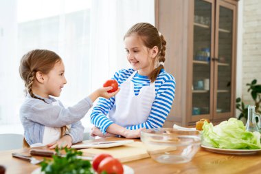 Ripe domates geçen süre pişirme lezzetli salata birlikte büyük kız kardeşi, mutfak iç arka plan üzerinde önlük giyen sevimli küçük kız