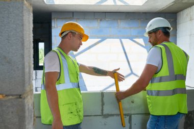 Kavganın ve Beton taş duvar düzeyi kontrol yansıtıcı yelek giyen iki inşaat işçileri portresi