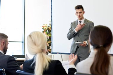 Ön planda izleyici ile konferans salonunda beyaz ekran tarafından sunum ayakta veren başarılı genç işadamı portresi