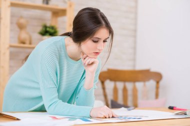 Dalgın genç tasarımcı düşünme iddialı proje, studio iç arka plan üzerinde ise ahşap masa üzerine eğilerek örme kazak giyiyor