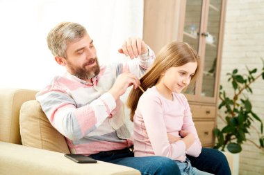 Sevgi dolu orta yaşlı babam penye saç oldukça küçük kızı rahat oturma odasında otururken, Güneş ışınları ile aydınlatılmış