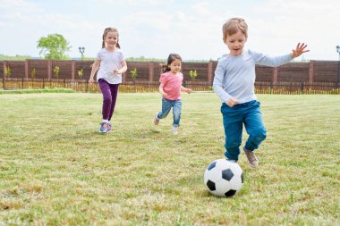 Yeşil çimenlerin üzerinde ön bahçesinde futbol oynayan üç mutlu küçük çocuklar tam uzunlukta portresi